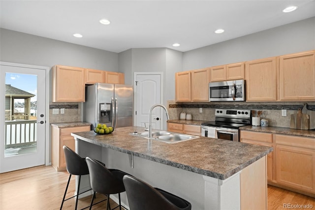 kitchen with appliances with stainless steel finishes, light brown cabinetry, a kitchen breakfast bar, an island with sink, and sink