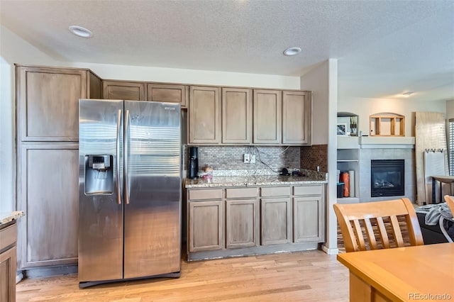 kitchen with decorative backsplash, light hardwood / wood-style floors, stainless steel refrigerator with ice dispenser, light stone countertops, and a textured ceiling