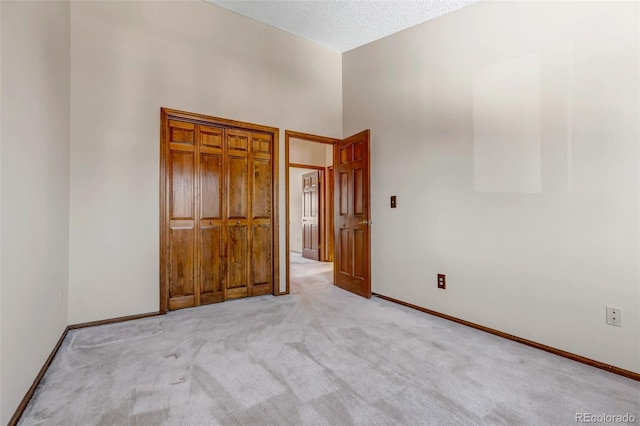 unfurnished bedroom with a high ceiling, light colored carpet, and a textured ceiling