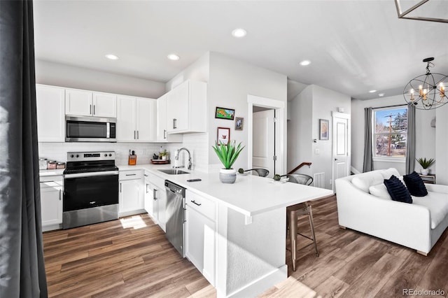 kitchen with decorative light fixtures, appliances with stainless steel finishes, a kitchen breakfast bar, and white cabinetry