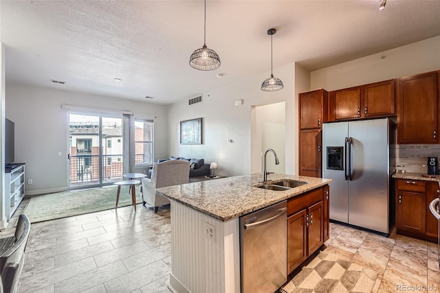 kitchen with light stone counters, appliances with stainless steel finishes, brown cabinetry, open floor plan, and a sink