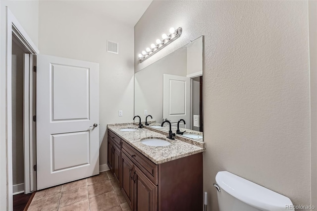 bathroom with toilet, double vanity, a sink, and visible vents