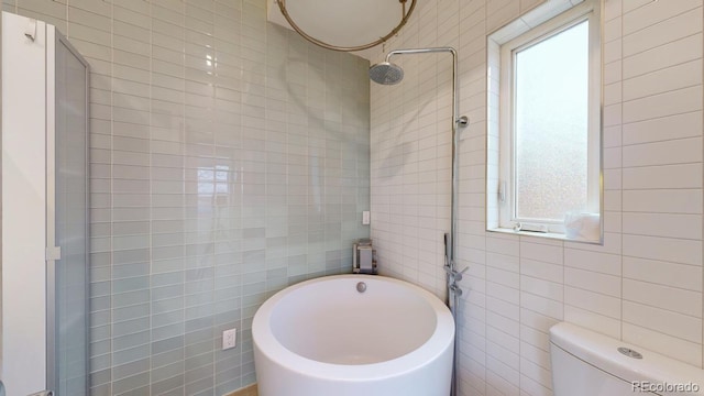 bathroom with toilet, a healthy amount of sunlight, and tile walls