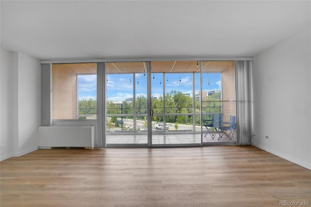 unfurnished room featuring radiator, wood finished floors, baseboards, and expansive windows