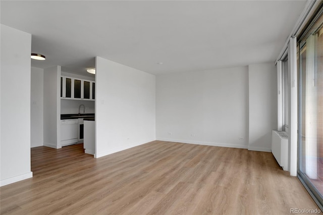 empty room with light wood finished floors, radiator, baseboards, and a sink