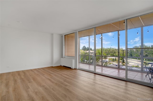 unfurnished room featuring a wall of windows, radiator heating unit, wood finished floors, and baseboards