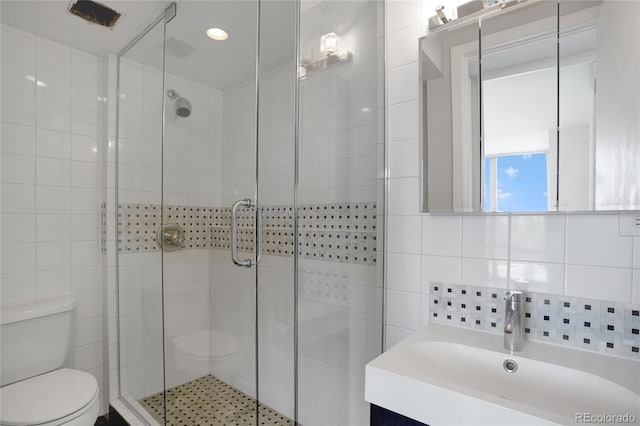 bathroom with vanity, tile walls, toilet, and a stall shower