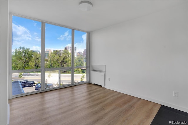 unfurnished room featuring baseboards, floor to ceiling windows, radiator heating unit, wood finished floors, and a view of city