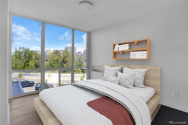 bedroom featuring a city view, a wall of windows, wood finished floors, and baseboards