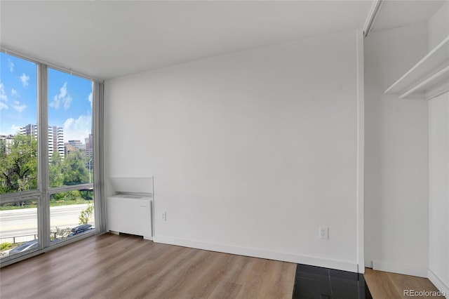 empty room featuring a wall of windows, baseboards, wood finished floors, and radiator heating unit