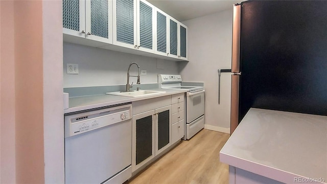 kitchen with light wood finished floors, light countertops, white cabinets, white appliances, and a sink