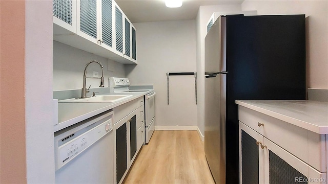 kitchen featuring white appliances, light countertops, light wood finished floors, and a sink