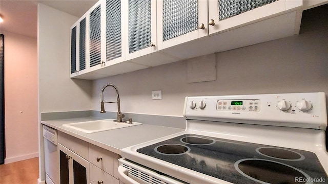 kitchen featuring a sink, wood finished floors, white cabinetry, white appliances, and light countertops