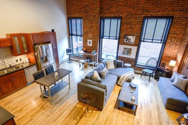 living area with a wealth of natural light, brick wall, baseboards, and wood finished floors