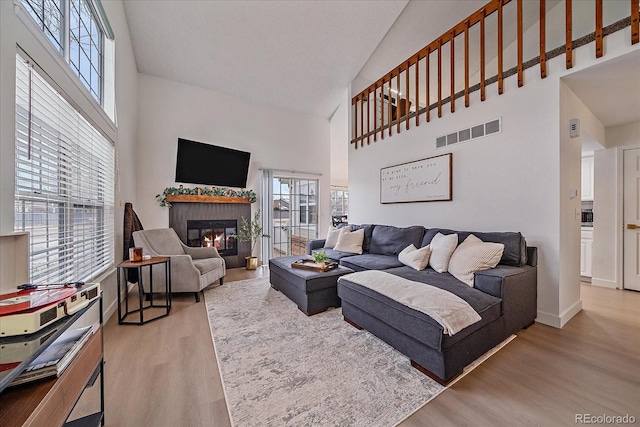 living area with visible vents, a glass covered fireplace, wood finished floors, a high ceiling, and baseboards