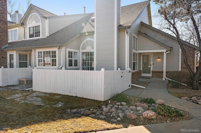 view of front of property with a shingled roof, brick siding, a fenced front yard, and a chimney