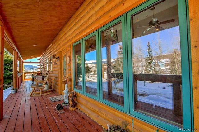 snow covered deck featuring a mountain view, a porch, and ceiling fan