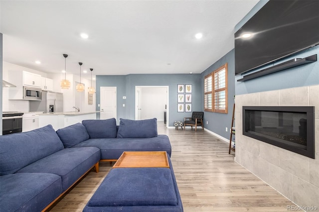 living room featuring recessed lighting, baseboards, a tiled fireplace, and light wood finished floors