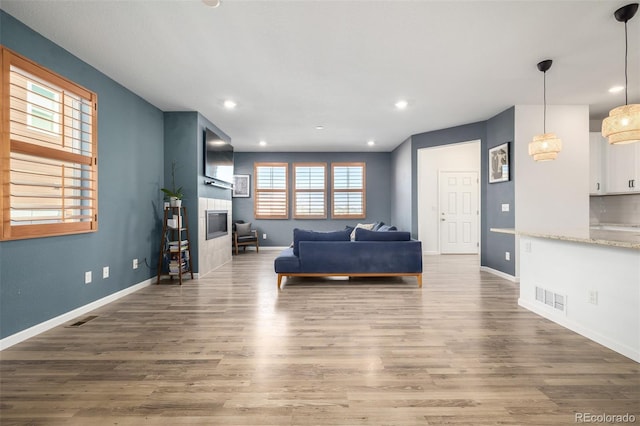 living room featuring a tiled fireplace, visible vents, baseboards, and wood finished floors