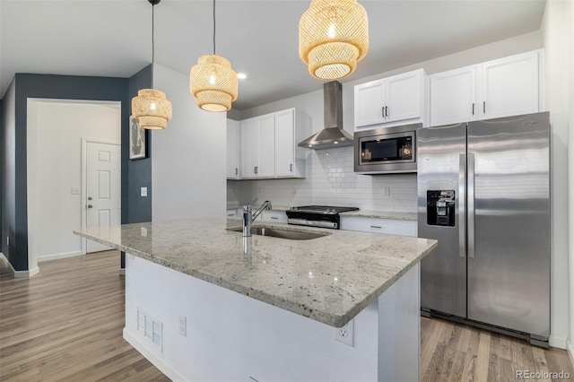 kitchen featuring light wood-style flooring, a sink, decorative backsplash, stainless steel appliances, and wall chimney range hood