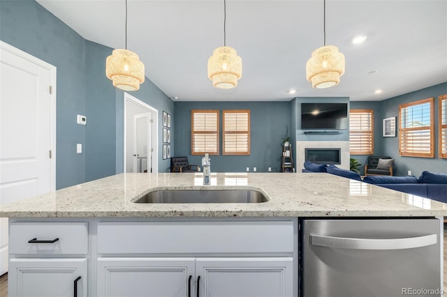 kitchen with a sink, open floor plan, a glass covered fireplace, white cabinetry, and stainless steel dishwasher