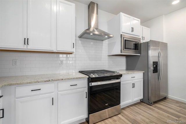 kitchen with light wood-type flooring, decorative backsplash, appliances with stainless steel finishes, white cabinets, and wall chimney exhaust hood