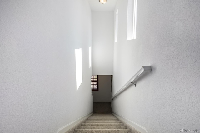 staircase featuring a textured wall, baseboards, and carpet floors