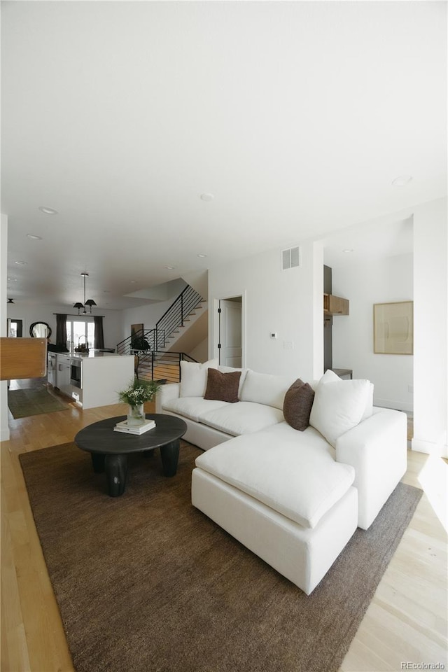 living area featuring visible vents, light wood finished floors, and stairs