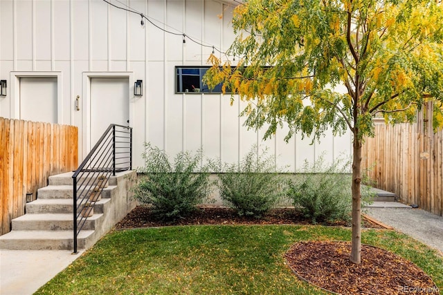 doorway to property with board and batten siding, fence, and a lawn