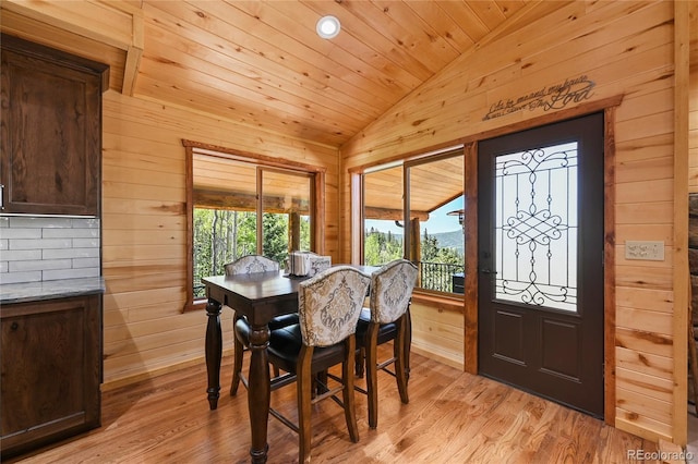 dining room featuring lofted ceiling, light wood-style floors, wood ceiling, and wooden walls