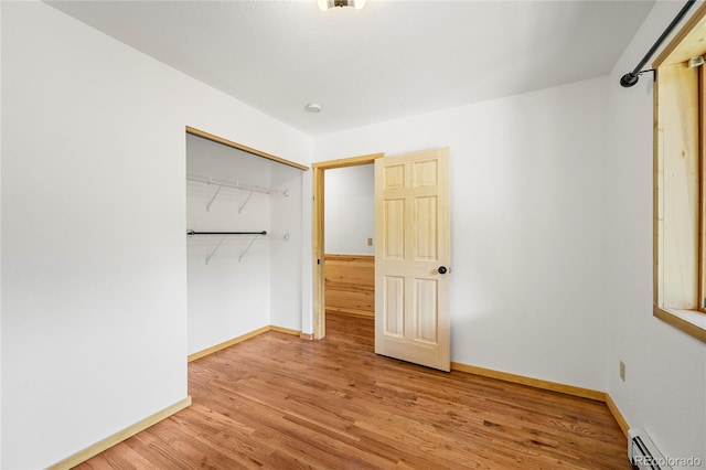 unfurnished bedroom with a baseboard heating unit, a closet, wood finished floors, and baseboards