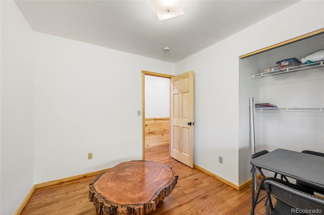 interior space with light wood-type flooring, a textured ceiling, and baseboards