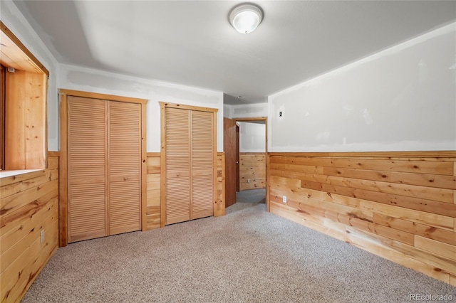 unfurnished bedroom with wainscoting, two closets, carpet flooring, and wooden walls