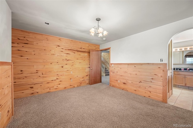 empty room with a chandelier, arched walkways, light carpet, and wooden walls