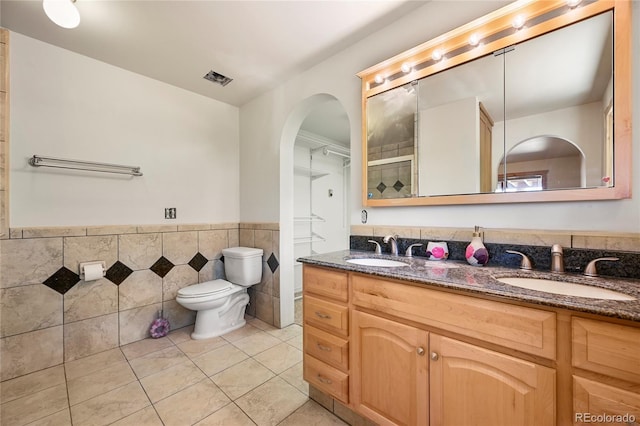 full bathroom featuring toilet, tile patterned flooring, tile walls, and a sink