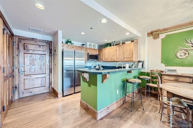 kitchen featuring a kitchen bar, light brown cabinets, light wood-type flooring, kitchen peninsula, and stainless steel appliances