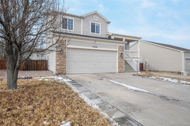 view of front of house with stone siding, stairway, concrete driveway, and fence