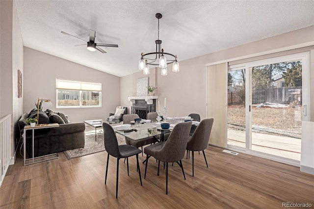 dining room with lofted ceiling, a textured ceiling, a fireplace, and wood finished floors