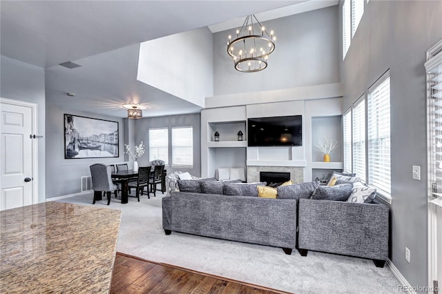 living room with hardwood / wood-style flooring, a fireplace, an inviting chandelier, and built in shelves