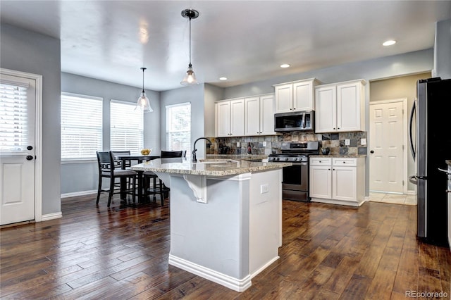 kitchen featuring appliances with stainless steel finishes, white cabinetry, backsplash, and hanging light fixtures