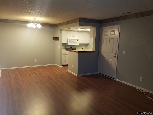 kitchen with white cabinets, white microwave, dark wood-type flooring, an inviting chandelier, and a textured ceiling