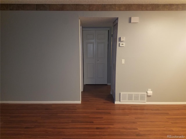 empty room with visible vents, a textured ceiling, baseboards, and wood finished floors