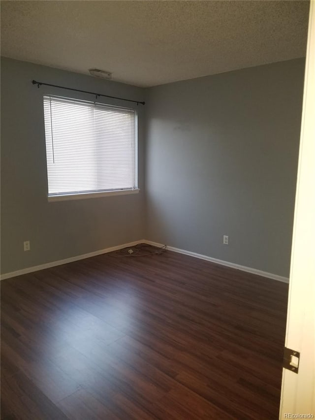 unfurnished room with dark wood-style floors, a textured ceiling, visible vents, and baseboards