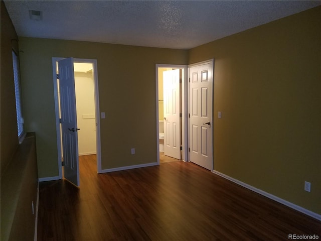 unfurnished bedroom with a walk in closet, a textured ceiling, baseboards, and wood finished floors