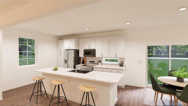 kitchen featuring white cabinets, stainless steel appliances, a kitchen breakfast bar, dark hardwood / wood-style floors, and a center island with sink