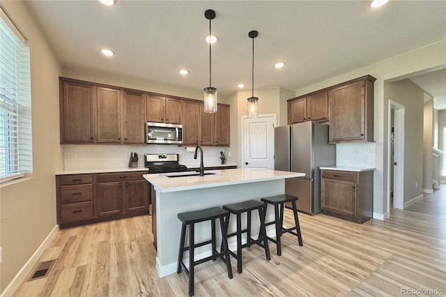 kitchen with a kitchen island with sink, stainless steel appliances, sink, light hardwood / wood-style floors, and pendant lighting