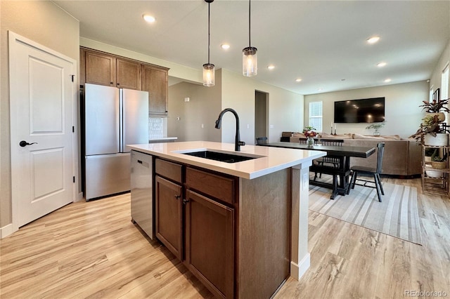 kitchen featuring appliances with stainless steel finishes, a center island with sink, sink, and light wood-type flooring