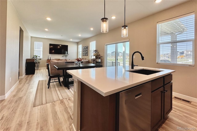 kitchen with a center island with sink, light wood-type flooring, dark brown cabinetry, and pendant lighting