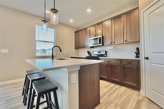 kitchen with decorative light fixtures, a center island with sink, light wood-type flooring, gas stove, and decorative backsplash