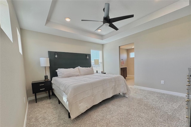 bedroom with ceiling fan, a tray ceiling, connected bathroom, and light colored carpet